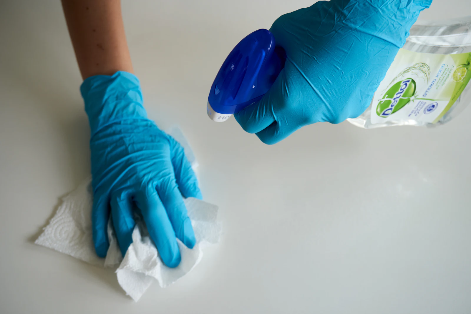Gloved hand wiping a counter with spray cleaner